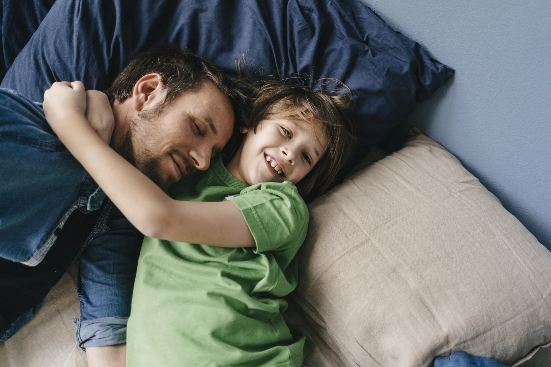 Ein Vater liegt ganz entspannt mit seinem Sohn auf dem Bett. Er vertraut auf die festen Zinsen des Plus Sparbriefs.